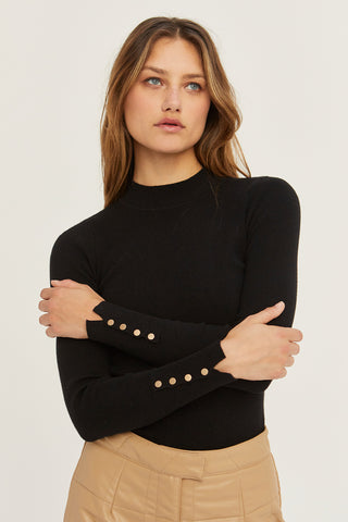 A woman wearing a black knit top with sleeve gold snap button detail.