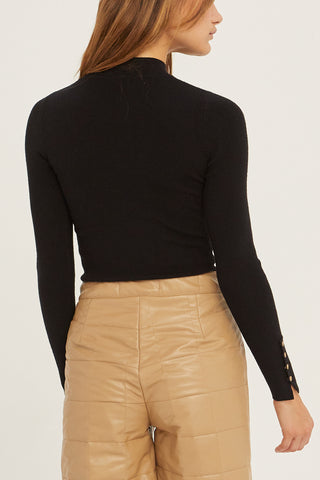 A woman wearing a black knit top with sleeve gold snap button detail.