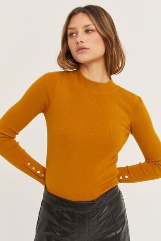 A woman wearing a mustard knit top with sleeve gold snap button detail.