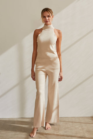 A model wearing a cream sleeveless turtleneck knit top with matching pants.