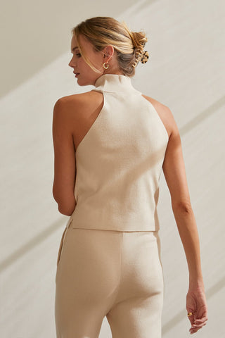 A model wearing a cream sleeveless turtleneck knit top with matching pants.