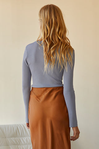 A model wearing a dusty blue long sleeve knit top with slit detail on sleeve.