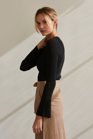 A model wearing a black long sleeve knit top with slit detail on sleeve.