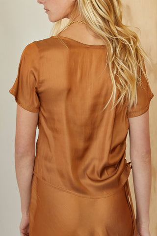 A model wearing a brown short sleeve satin blouse with tunnel ruching detail on one side.
