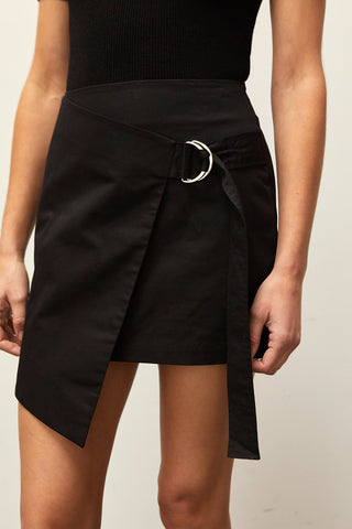 A woman wearing a black asymmetrical wrap mini skirt with D-ring detail.