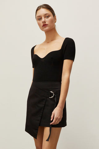 A woman wearing a black asymmetrical wrap mini skirt with D-ring detail.