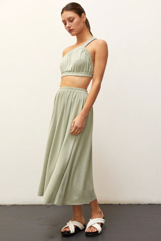 A woman wearing a sage one shoulder two piece set.