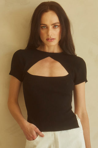 A woman wearing a black short sleeve knit top with cut out detail at front chest.