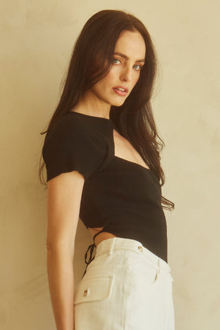 A woman wearing a black short sleeve knit top with cut out detail at front chest.