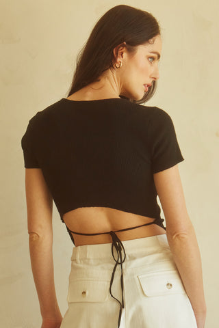 A woman wearing a black short sleeve knit top with cut out detail at front chest.