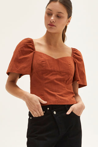 A woman wearing a rust backless with laced up straps top.