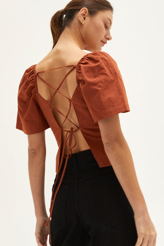 A woman wearing a rust backless with laced up straps top.