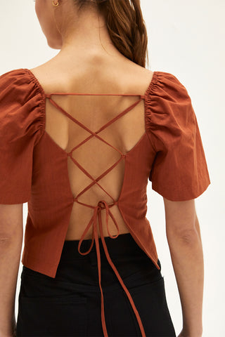 A woman wearing a rust backless with laced up straps top.