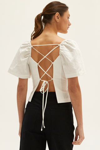 A woman wearing an ivory backless with laced up straps top.