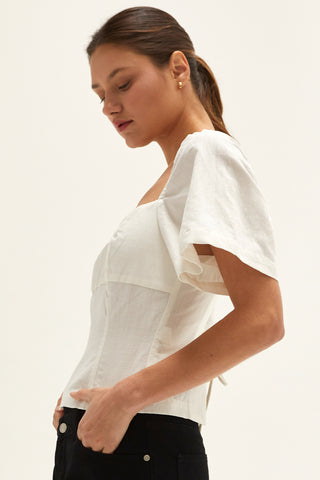 A woman wearing an ivory backless with laced up straps top.