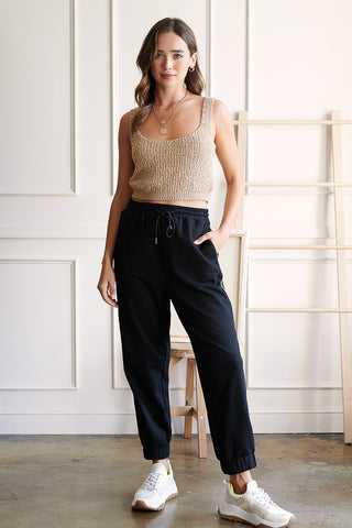 A woman wearing a sand knitted tank top and a black boyfriend jogger pants.